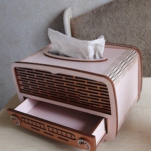 Könnte beinhalten: Ein rosa und brauner Holz-Tischtuchhalter mit Schublade. Der Tischtuchhalter ist in Form eines Vintage-Radios gestaltet.