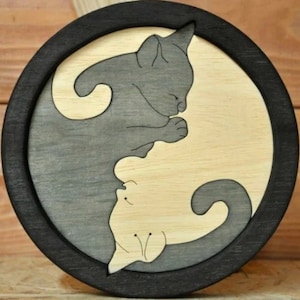 Może przedstawiać: Okrągłe drewniane pudełko z czarną ramką i wzorem yin yang przedstawiającym dwa koty. Jeden kot jest szary, a drugi biały.