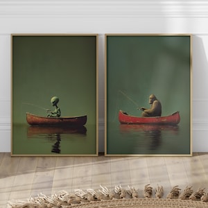 May include: Two framed art prints. One shows an alien fishing from a red canoe, the other a Bigfoot figure fishing from a red canoe. Both are set against a green background, with reflections in the water.