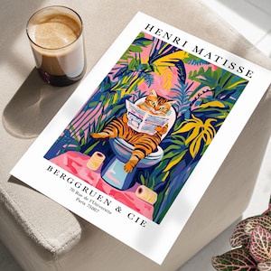 Op de afbeelding: Een kleurrijke kunstprint met een kat die een krant leest op een toilet, tegen een jungle-achtige achtergrond. De print bevat de tekst "HENRI MATISSE" en "BERGGRUEN & CIE". Een kopje koffie staat ernaast.
