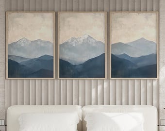 May include: Three framed landscape paintings with a muted color palette of blue and beige. The paintings depict a mountain range with a snowy peak in the distance.