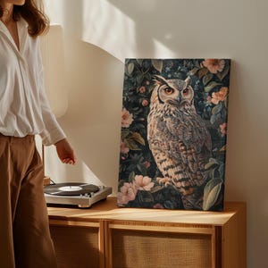 May include: A canvas print featuring a detailed illustration of an owl perched in a lush garden setting. The owl has large, bright yellow eyes and intricate brown and white feathers. The background is a dark green with pink flowers and leaves.