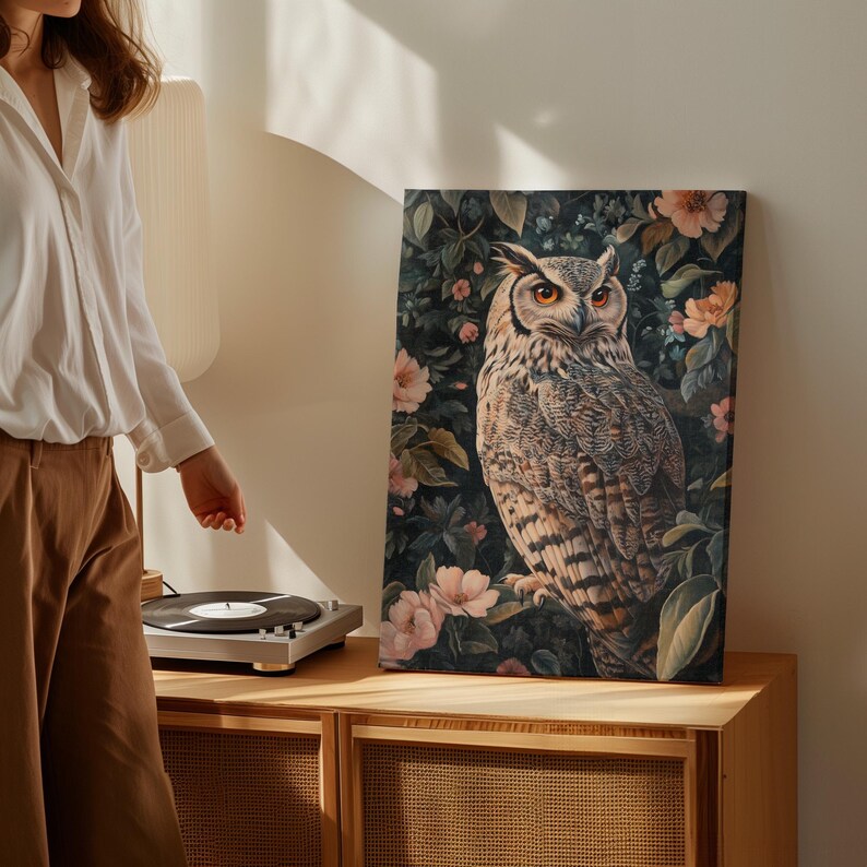 May include: A canvas print featuring a detailed illustration of an owl perched in a lush garden setting. The owl has large, bright yellow eyes and intricate brown and white feathers. The background is a dark green with pink flowers and leaves.