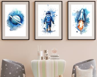 May include: Three watercolor paintings in black frames. The first painting shows a blue planet with rings in a blue and white nebula. The second painting shows an astronaut in a blue spacesuit walking away from the viewer. The third painting shows a white rocket ship with orange flames launching into a blue and white nebula.
