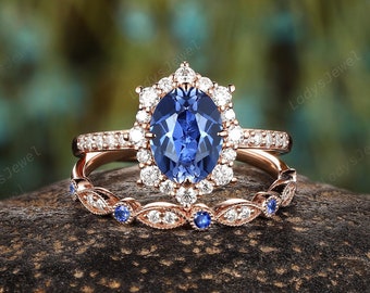 May include: A rose gold engagement ring set with a large oval blue sapphire surrounded by smaller diamonds. The band is also set with smaller diamonds and has a matching wedding band with smaller blue sapphires.