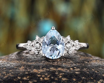 May include: A pear-shaped aquamarine engagement ring with a delicate floral design. The ring is set in white gold and features small diamonds on the band.