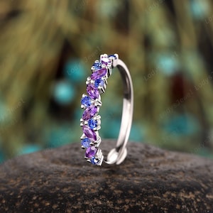 May include: A delicate silver band ring with a row of alternating amethyst and sapphire gemstones. The gemstones are set in a pave setting and are arranged in a graduated pattern.