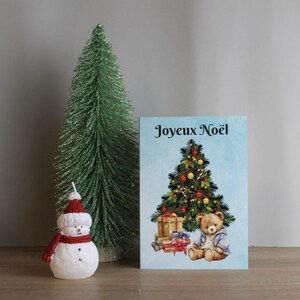 Weihnachtskarte auf französisch. Teddybär und Geschenke unterm Weihnachtsbaum. Karte von Noël in Französisch. Ours en peluche sous sapin de Noël.