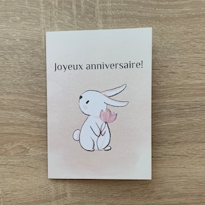 Karte zum Geburtstag in Frankreich. Lapis Mignon mit einer Rose. Geburtstagskarte auf Französisch, süßes Häschen mit rosa Blume.