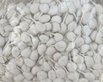 Puede incluir: Una bolsa de plástico transparente llena de numerosas mechas de algodón blancas. Cada mecha tiene una cabeza de algodón redondeada y un tallo delgado blanco. Las mechas están densamente empaquetadas, creando una apariencia llena y texturizada.