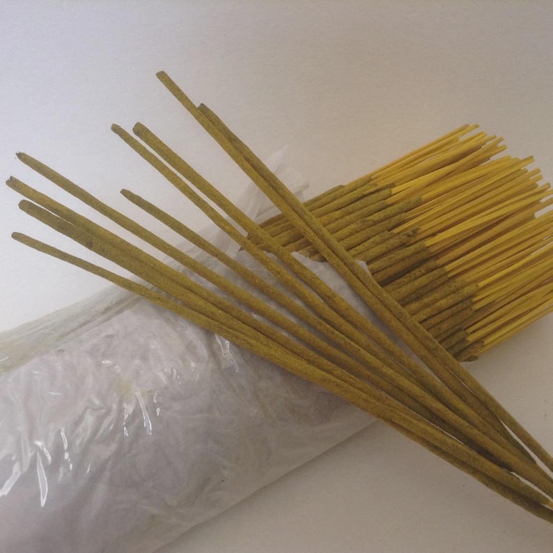 Puede incluir: Un conjunto de varillas de incienso de color amarillo, dispuestas en forma de abanico. Las varillas delgadas parecen estar hechas de materiales naturales. Una bolsa de pl&aacute;stico blanca es parcialmente visible, lo que sugiere embalaje.