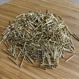 May include: A large pile of gold-colored tacks or thumbtacks on a wooden surface.