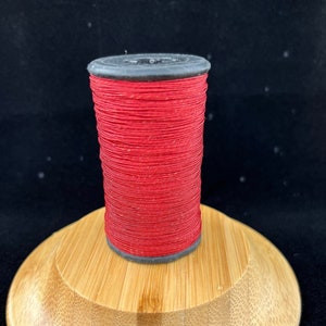 May include: A spool of red thread on a wooden stand. The thread is wound tightly and has a smooth, even texture.
