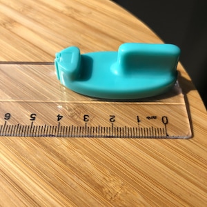 Puede incluir: Una regla de plástico turquesa con una regla de plástico transparente debajo. La regla está marcada con números del 0 al 9.