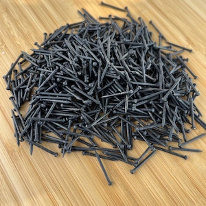 Puede incluir: Un montón de tachuelas de metal negro sobre una superficie de madera.