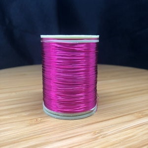 Può includere: Un rocchetto di filo metallico rosa brillante, avvolto strettamente su un'anima di plastica bianca.