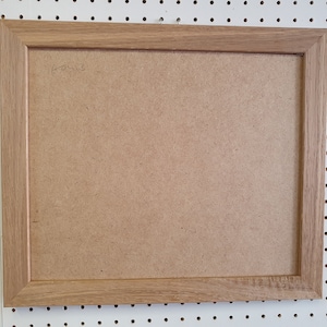 May include: A natural wood picture frame with a light brown finish. The frame is empty and ready to display a photo or artwork.