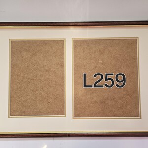 May include: A brown wooden picture frame with a gold trim. The frame has two openings for photos. The frame has a white mount and the text "L259" is printed on the bottom right opening.