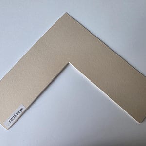 以下が含まれることがあります： V字型の開口部があるベージュ色のマット。マットはテクスチャ加工された表面で、隅には「SW16 Beige」と書かれたラベルが付いています。アートワークや写真をフレーミングするために設計されています。