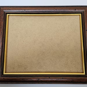 May include: A brown wooden picture frame with a gold trim. The frame is empty and ready for a photo or artwork.