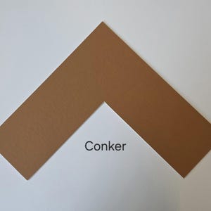 May include: A brown picture mount with a white interior and a V-shaped aperture. The word "Conker" is printed in black on the white interior. The mount is set against a white background.