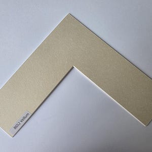 以下が含まれることがあります： V字型の、オフホワイトのマットボード。表面はテクスチャ加工が施されています。マットボードは長方形で、中央に切り抜きがあります。隅のラベルには「8652 Vellum」と書かれています。