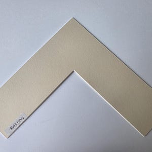 以下が含まれることがあります： V字型の開口部があるアイボリー色のマット。マットはテクスチャ加工された表面で、左下隅に「8043 Ivory」と書かれたラベルが付いています。 写真やアートワークのフレーミングに最適です。