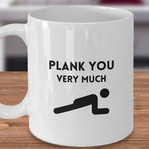 May include: White ceramic coffee mug with a black silhouette of a person doing a plank exercise and the text "Plank You Very Much".