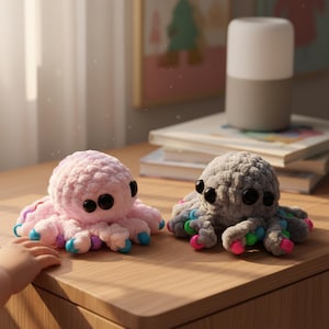May include: Two crocheted octopus toys. One is pink with blue, purple, and green accents on its tentacles. The other is gray with similar colorful accents. Both have large black eyes and are sitting on a wooden surface.