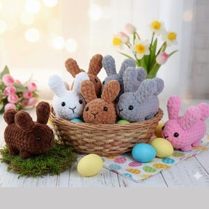 May include: A selection of handmade crochet bunnies in a wicker basket and on a white surface. The bunnies are in various colours, including white, brown, and grey. Easter eggs and flowers are also present, creating a festive scene.