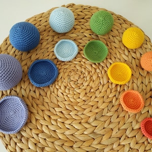 May include: A set of 10 crocheted balls and bowls in various colors, including blue, green, yellow, and orange. The balls and bowls are arranged in a circle on a woven straw mat.