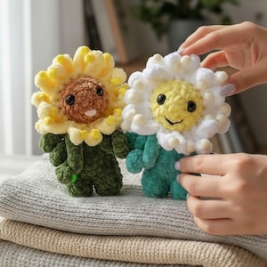 May include: Two handmade crochet flower dolls. One is a sunflower with yellow petals and a brown centre, the other is a daisy with white petals and a yellow centre. Both have smiling faces and green bodies.