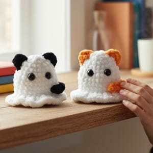 Könnte beinhalten: Zwei handgefertigte gehäkelte Tierfiguren. Eine ist weiß mit schwarzen Ohren und einer schwarzen Nase, die andere ist weiß mit orangefarbenen Ohren und einer kleinen orangefarbenen Pfote. Beide haben schwarze Knopfaugen und sitzen auf einer Holzoberfläche.