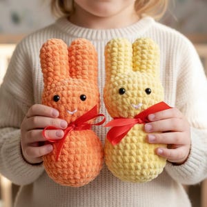 Puede incluir: Dos conejos de crochet hechos a mano, uno naranja y otro amarillo. Cada uno tiene ojos negros, una sonrisa cosida y una cinta roja alrededor del cuello. Estos conejos de peluche son ideales para Pascua o como juguete infantil.