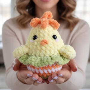 May include: A handmade crochet chick toy in yellow, orange, and green. The chick has black eyes, a small orange beak, and a tuft of orange yarn on its head. The chick is sitting on a green and orange base.