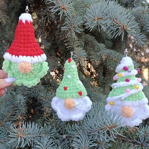 Könnte beinhalten: Drei gehäkelte Ornamente in Form von Gnomen. Die Gnomen tragen grüne Hüte und haben weiße Bärte. Die Ornamente sind mit Perlen verziert und hängen an einem Weihnachtsbaum.