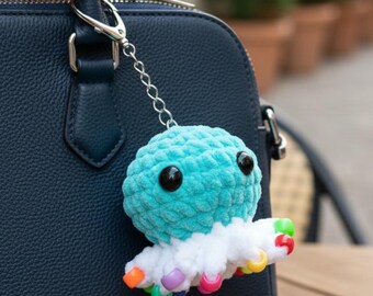 May include: A turquoise and white crocheted octopus keychain with black eyes and colorful tentacle tips. The plush toy is attached to a silver chain and clasp, hanging from a navy blue handbag.