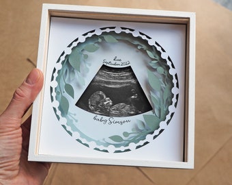 May include: A white frame with a green paper cut-out design around a black and white ultrasound image. The text "due September 2022" and "baby Simson" is written below the image.