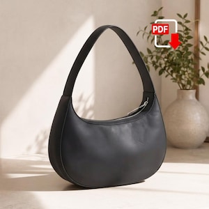 May include: A smooth black leather hobo bag with a curved crescent shape, a single integrated shoulder strap, and a silver-toned metal zipper closure along the top edge. The bag features a clean, solid-colored exterior with minimal detailing.