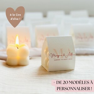Könnte beinhalten: Weiße Hochzeitsgeschenkkästchen mit einem personalisierten Design mit den Namen "Morgene & Arthur" und dem Datum "Samedi 14 Aout 2030". Die Kästchen sind mit kleinen weißen Kerzen in Form von Schmetterlingen gefüllt.