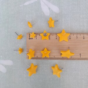 Three pairs of yellow star shaped stud earrings in small, medium and large with a wooden ruler and green background with white dragonflies
