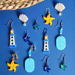 May include: Assortment of colorful earrings featuring seashells, lighthouses, starfish, and other nautical themes. The earrings are displayed on a blue background.