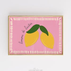May include: A framed print featuring two yellow lemons with green leaves on a pink background. The words "limoni di Sicilia" are written in cursive. The frame is gold and the print has a white dotted border.