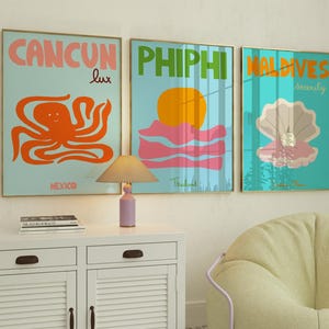 Puede incluir: Tres carteles de viaje coloridos con ilustraciones de un pulpo, una puesta de sol sobre el agua y una concha. Los carteles están enmarcados en oro y tienen las palabras "Cancun lux", "Phi Phi Tailandia" y "Maldives serenity" en ellos.