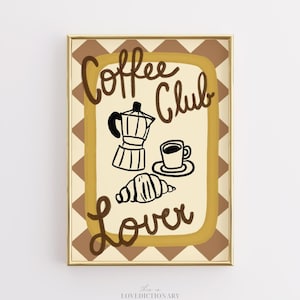 May include: A framed print with a gold border featuring the words "Coffee Club Lover" in brown script. The image includes a black coffee pot, a cup of coffee, and a croissant on a light brown background.