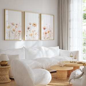 May include: Three framed watercolor paintings of delicate pink and orange flowers with green stems and leaves on a white background. The frames are gold and the paintings are hanging on a white wall.