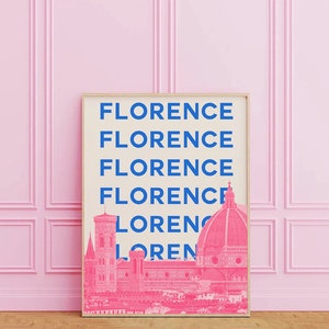 May include: A framed print with the word "Florence" repeated five times in blue text on a cream background. The bottom of the print features a pink silhouette of the Florence skyline, including the Duomo.