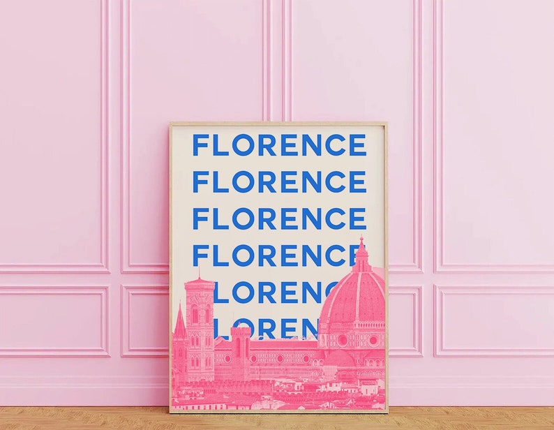 May include: A framed print with the word "Florence" repeated five times in blue text on a cream background. The bottom of the print features a pink silhouette of the Florence skyline, including the Duomo.