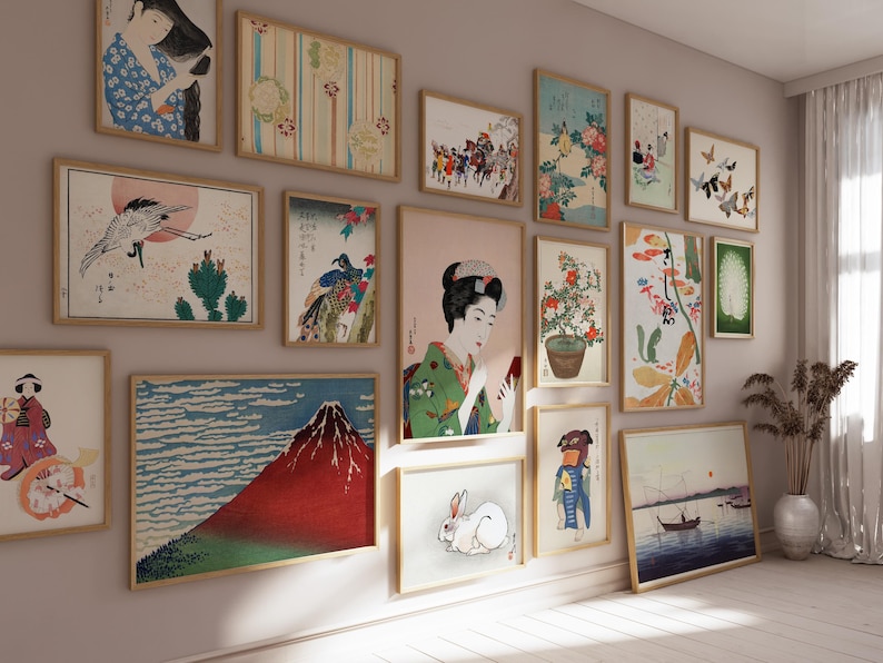 May include: A wall gallery featuring a collection of framed Japanese art prints. The prints depict various scenes, including a woman in traditional clothing, a mountain landscape, and a bird in flight. The prints are arranged in a grid pattern on a light-colored wall.