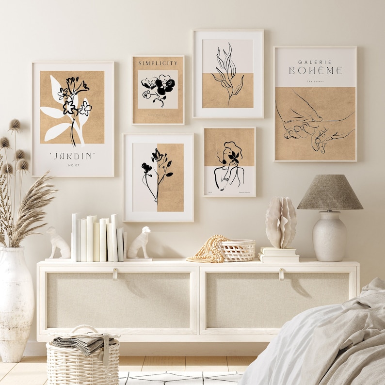 May include: A set of six minimalist black and white line art prints with a beige background. The prints feature various designs including flowers, leaves, a woman, and hands. The prints are framed in white and are displayed on a white wall above a white dresser.